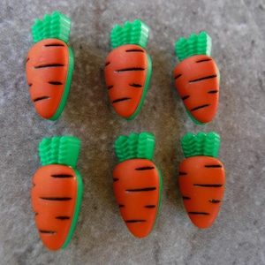 May include: Six orange carrot-shaped buttons with green tops. The buttons are made of plastic and have a glossy finish.