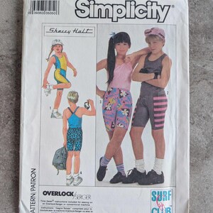 May include: Vintage Simplicity sewing pattern featuring children's swimwear designs. The pattern includes illustrations of various swimsuits and shorts. The package has the "Simplicity" logo and the text "Surf Club".