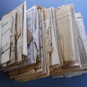 May include: A stack of vintage sewing patterns in various sizes and colors. The patterns are made of paper and have been folded and stored for many years. The patterns are in various states of wear and tear, with some being more faded and worn than others. The patterns are a great source of inspiration for vintage clothing and craft projects.