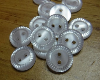 May include: A pile of white plastic buttons with two holes each. The buttons have a raised, textured edge.