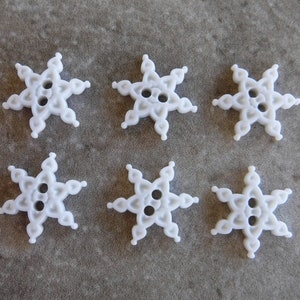 May include: Six white snowflake-shaped buttons with a raised design. The buttons have two holes each.