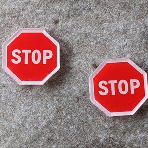May include: Two red stop signs with white lettering and a white border. The signs are on a gray background.
