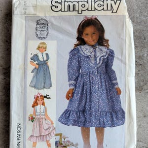 May include: Simplicity sewing pattern featuring a girl's dress design. The pattern includes illustrations of the dress in blue and pink, with white lace trim. The pattern number is 7407.