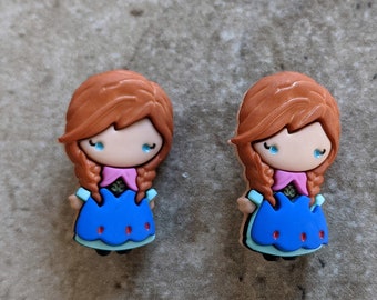 May include: Two small plastic figurines of a girl with brown hair, blue eyes, and a blue dress. The girl is wearing a pink scarf and has a braid on each side of her head.