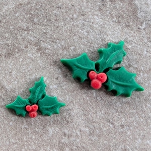 May include: Two green holly sprigs with red berries. The leaves have a glossy finish, and the berries are clustered together. These festive decorations are perfect for holiday crafts and embellishments.