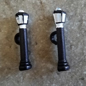 May include: Two black metal lamp post buttons with white glass lampshades. The lamp posts are about 2 inches tall.