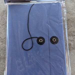 May include: A blue accordion keeper made of paper with a black string and two metal eyelets. The packaging says "Bazzill Basics Paper" and "bazzill accordion keeper".