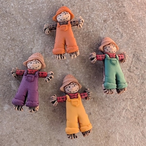 May include: Four small, colorful scarecrow figurines with straw hats, overalls, and plaid shirts. The scarecrows are made of plastic and have a whimsical, cartoon-like appearance.
