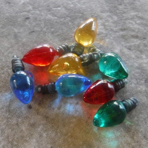 May include: A group of eight miniature light bulbs in various colors, including red, blue, green, and yellow. The bulbs are strung together with black wire and are perfect for adding a festive touch to any craft project.