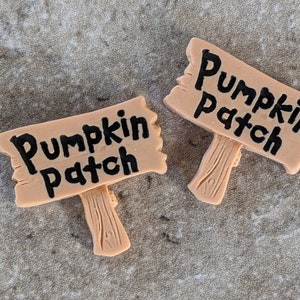 May include: Two brown wooden signs with black lettering that reads "Pumpkin Patch".