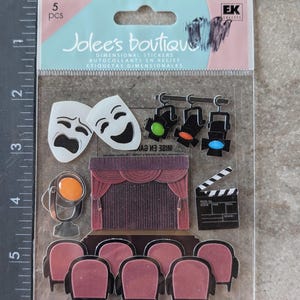 May include: A package of 5 dimensional stickers featuring theater-themed designs. The stickers include comedy and tragedy masks, stage lights, a stage with curtains, a film clapperboard, and rows of theater seats. The package is labeled "Jolee's Boutique".