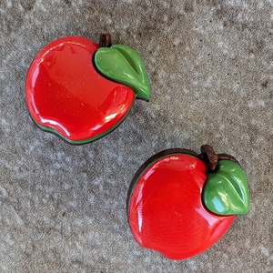 May include: Two red plastic apple-shaped objects with green leaves. The apples are shiny and have a smooth surface.