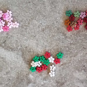 May include: Assortment of colorful plastic buttons in the shape of a five-pointed star. The buttons are pink, red, green, white, and brown.