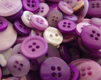 May include: A collection of purple and white buttons of various sizes and styles. The buttons are made of plastic and have a smooth, shiny finish.