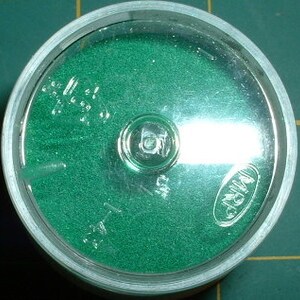 May include: A small, round, clear plastic container with a green, textured surface inside. The container has a clear lid and a small, silver button in the center. The text "WINDSOR" is printed on the lid.