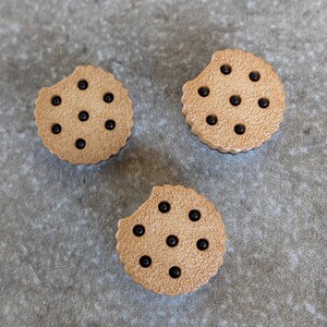 May include: Three brown cookie-shaped buttons with black dots. The buttons are made of plastic and have a textured surface.