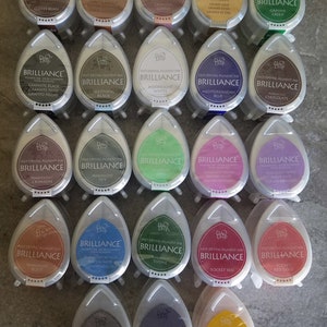 May include: A collection of 20 ink pads in various colors, each with the words "Fast Drying Pigment Ink" and "Brilliance" printed on the front. The ink pads are arranged in four rows of five, with each row featuring a different color scheme.