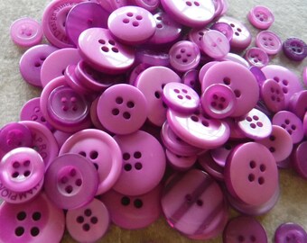 May include: A large assortment of purple plastic buttons of various sizes and styles. Some buttons have four holes, while others have two holes. Some buttons have a shiny finish, while others have a matte finish.