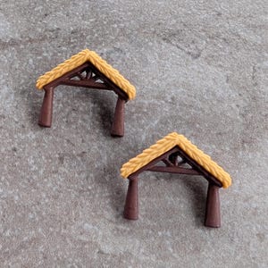 May include: Two miniature brown archway structures with tan thatched roofs. The archways have a triangular roof design and are made of a dark brown material. The thatched roofs are a light tan color.