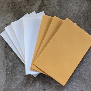 May include: A stack of white envelopes and a stack of brown envelopes. The envelopes are all the same size and shape.