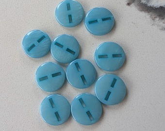 May include: A collection of ten light blue, round buttons. Each button has two rectangular slots cut into the surface. The buttons are scattered on a light-colored surface.