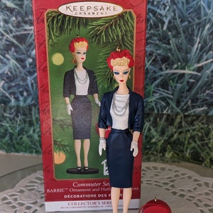 May include: A Hallmark Keepsake ornament featuring a Barbie doll dressed in a blue skirt suit with a white blouse and red hat. The ornament is part of a set of two and is labeled "Commuter Set".