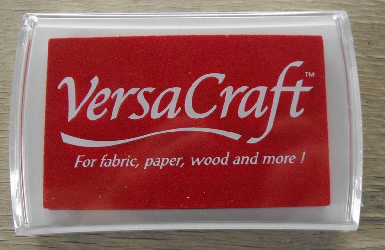 May include: A red ink pad with the text "VersaCraft&trade;" in white lettering. The ink pad is labeled "For fabric, paper, wood and more!"
