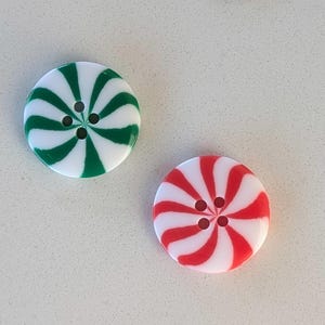 May include: Two round buttons with a peppermint candy design. One button has green and white stripes, and the other has red and white stripes. Each button has four small holes in the center for sewing.