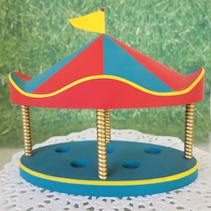 May include: A red and blue striped tent with a yellow flag on top. The tent has a gold base with four holes in the top. The base is blue with a yellow trim.