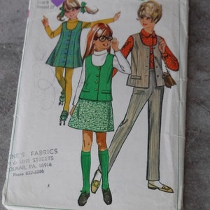 May include: Vintage Simplicity sewing pattern number 7838 for girls' clothing. The pattern includes three outfits: a green plaid dress with a vest, a green skirt with a vest, and a striped pantsuit with a vest. The pattern is for sizes 8-14 and has a bust measurement of 27 inches.