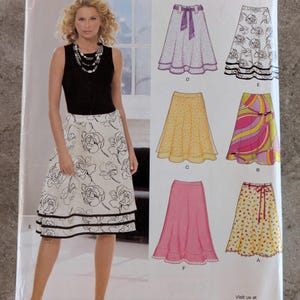 May include: A sewing pattern from New Look featuring various skirt designs. The cover shows a woman wearing a black top and a white skirt with a floral print. The pattern includes options for different skirt styles and sizes A 10-22.