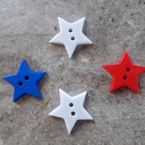 May include: Four star-shaped buttons in red, white, and blue. Each button has two holes for sewing. The buttons are arranged on a gray surface, with a glossy finish.