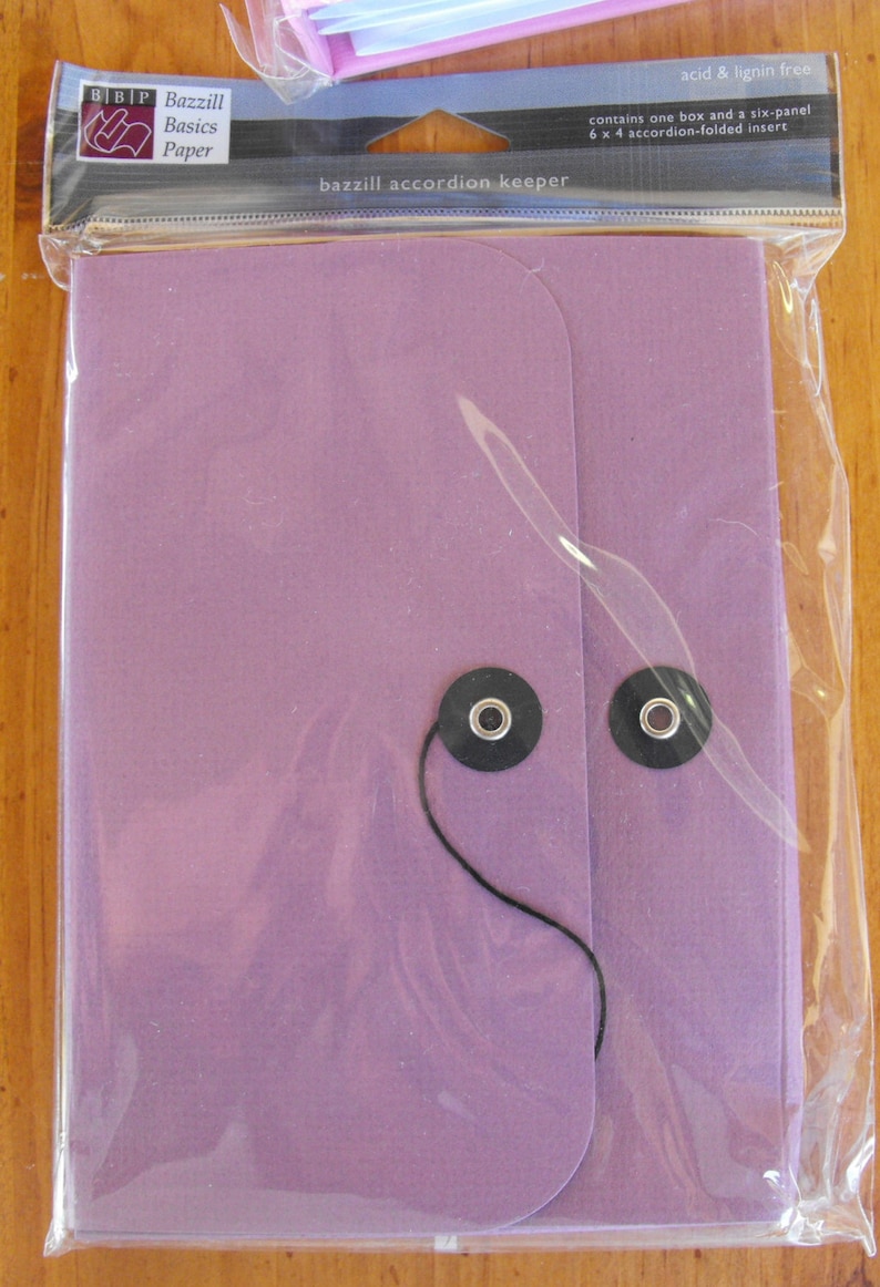May include: A purple accordion keeper with a black string and two black buttons. The packaging says "Bazzill Basics Paper" and "bazzill accordion keeper".