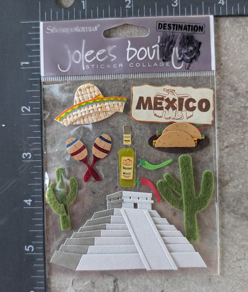 May include: A sticker collage featuring Mexican-themed designs. Includes a sombrero, the word "MEXICO", maracas, a tequila bottle, tacos, cacti, and a pyramid. The package is labeled "Jolee's Boutique Sticker Collage".