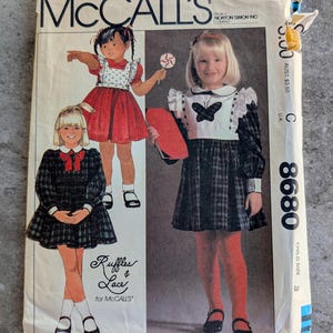 May include: Vintage McCall's sewing pattern envelope featuring illustrations of little girls in dresses. The envelope has the text "McCall's" at the top, with the words "Ruffles & Lace" and the pattern number 8680. The envelope is slightly worn.