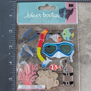 May include: A package of Jolee's Boutique dimensional stickers featuring underwater-themed designs. The stickers include blue and black flippers, a red and yellow snorkel, a blue and white diving mask, and various fish and coral. The package reads "10 PCS".