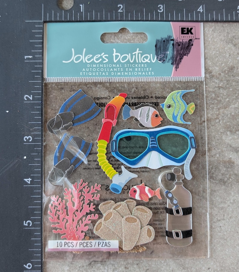 May include: A package of Jolee's Boutique dimensional stickers featuring underwater-themed designs. The stickers include blue and black flippers, a red and yellow snorkel, a blue and white diving mask, and various fish and coral. The package reads "10 PCS".