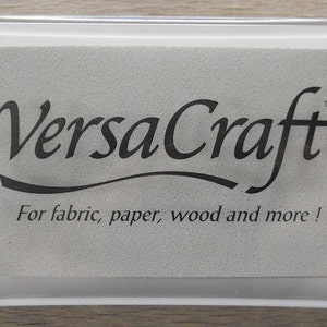 May include: A white ink pad with the text "VersaCraft&trade;" in black lettering. The text "For fabric, paper, wood and more!" is also printed in black below the logo.