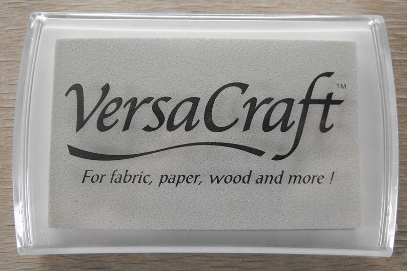 May include: A white ink pad with the text "VersaCraft&trade;" in black lettering. The text "For fabric, paper, wood and more!" is also printed in black below the logo.