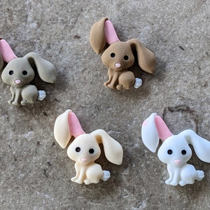 May include: Four felt bunny rabbit buttons with pink ears. Two are brown and two are white.