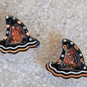 May include: Two black witch hat shaped ceramic ornaments with orange and white trim. The hats are filled with red and black beads.