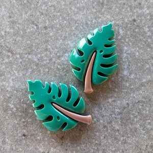May include: Two green plastic tropical leaf shaped earrings with a brown accent in the center of each leaf.