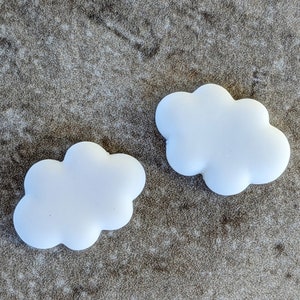 May include: Two white cloud-shaped decorations on a brown textured surface.