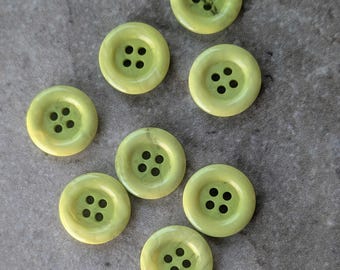 Puede incluir: Un conjunto de ocho botones redondos de color verde lima claro, cada uno con un acabado liso y brillante y cuatro orificios centrados para su fijación. Los botones están dispuestos en un patrón disperso, mostrando una forma circular uniforme.