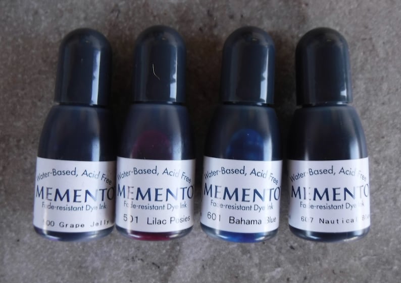 Puede incluir: Cuatro botellas peque&ntilde;as de tinta Memento resistente a la decoloraci&oacute;n en varios colores: Grape Jelly, Lilac Posies, Bahama Blue y Nautical Blue. Cada botella tiene una tapa gris oscuro y una etiqueta blanca con texto negro. La tinta es a base de agua y sin &aacute;cido.