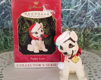 Könnte beinhalten: Hallmark Keepsake Ornament, Puppy Love Collector's Series, zeigt einen weißen Welpen, der einen roten Weihnachtsmann-Hut und einen roten Schal mit einem goldenen Herzanhänger trägt. Der Anhänger befindet sich in seiner Originalverpackung.