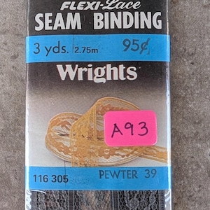 May include: A package of Flexi-Lace seam binding in pewter gray. The package includes 3 yards (2.75m) of lace trim. The label reads "SEAM BINDING" and "Wrights". A pink sticker with "A93" is attached.