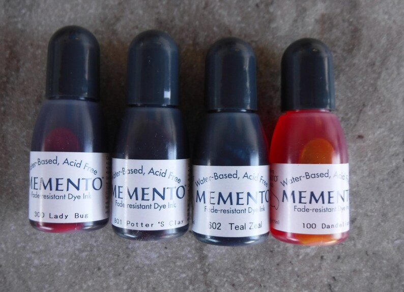 Puede incluir: Cuatro botellas peque&ntilde;as de tinta de tinte resistente a la decoloraci&oacute;n Memento en varios colores. Las botellas tienen tapas negras y etiquetas blancas con el nombre de la marca y los nombres de los colores: Lady Bug, Potter's Clay, Teal Zeal y Dandelion. La tinta es a base de agua y sin &aacute;cido.