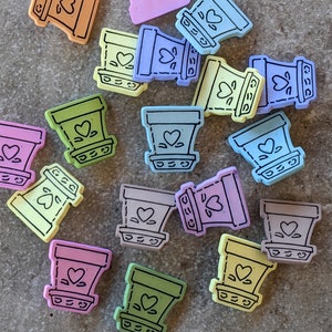 May include: A collection of 14 pastel-colored ceramic flower pots with a heart design and black outlines. The pots are in various colors, including pink, blue, green, yellow, and purple.