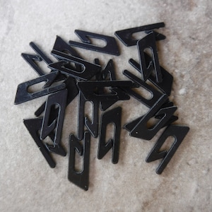 May include: A collection of small, black plastic clips scattered on a neutral-toned surface. Each clip has a unique shape with a rectangular body and a curved hook-like extension, suggesting they are designed for fastening or securing items.